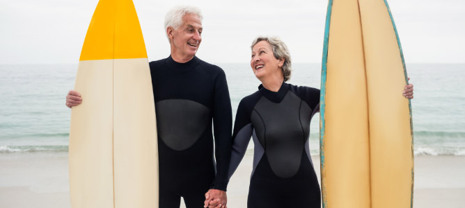Happy retired couple with surfboards at beach