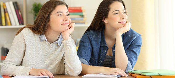 Two female students sitting at desk dreaming looking out window